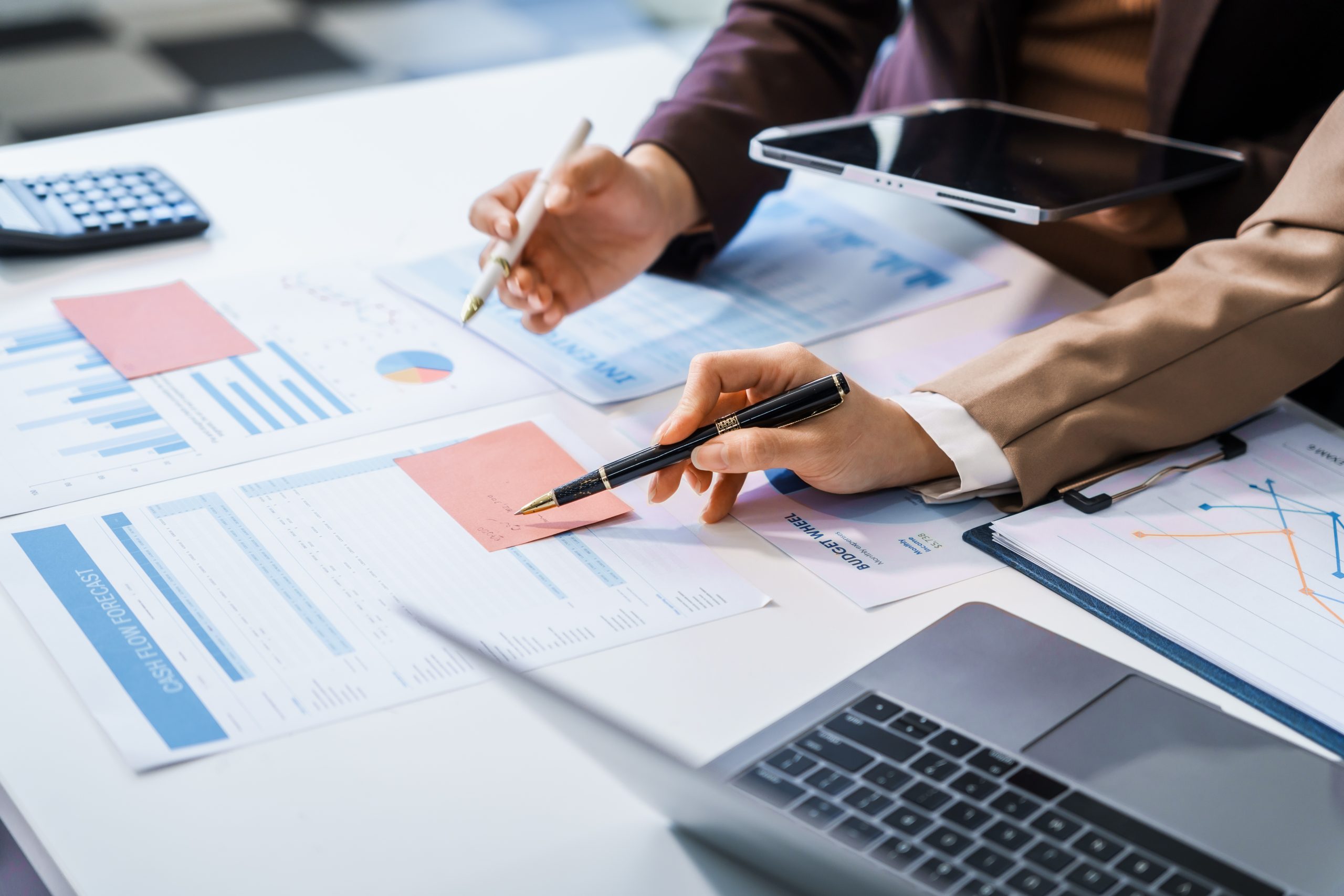 Hands of professionals reviewing financial charts and reports with pens and a tablet at a business meeting.