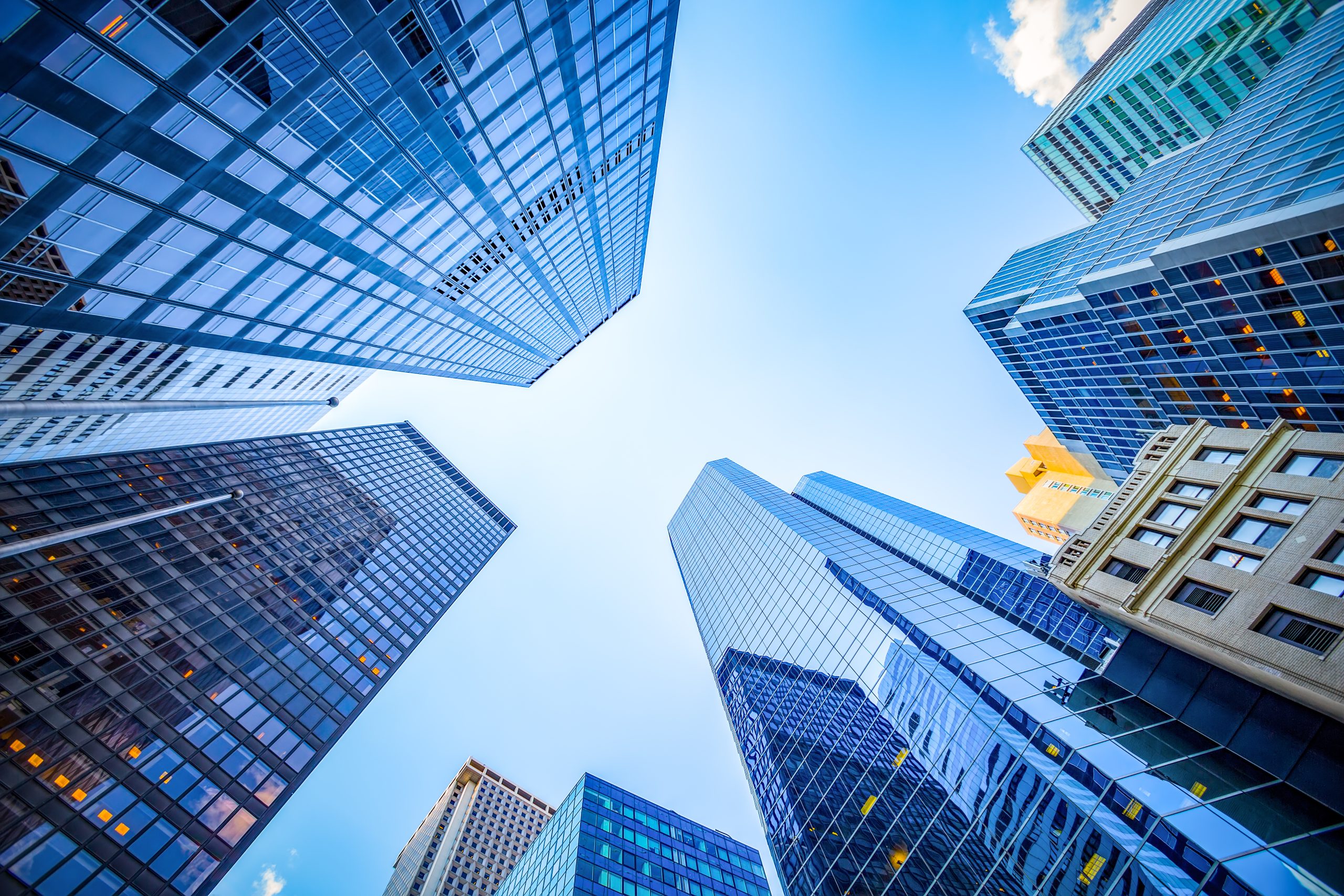 Upward view of glass skyscrapers in Manhattan financial district against a blue sky.